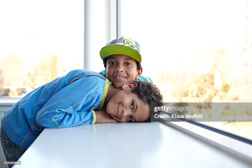 2 boys lies in window sill smiling to camera