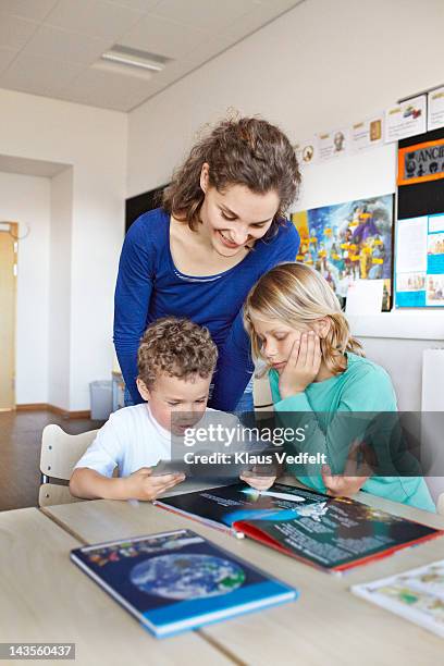 2 boys looking at tablet with teacher - teacher bending over stock-fotos und bilder