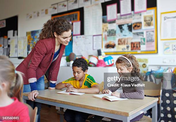 teacher looking in book with children - primary school teacher fotografías e imágenes de stock