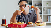 Asian fat man enjoy to eat unhealthy junk food, hamburger, pizza, fried chicken