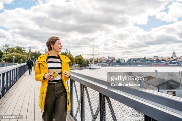 young woman using phone on the bridge in stockholm - yellow coat 個照片及圖片檔