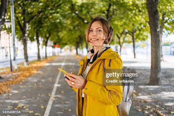 young woman using phone in the park in stockholm - yellow coat stock pictures, royalty-free photos & images