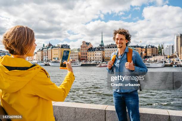 girlfriend taking a picture of her boyfriend on the quayside in stockholm - riverbank stock pictures, royalty-free photos & images