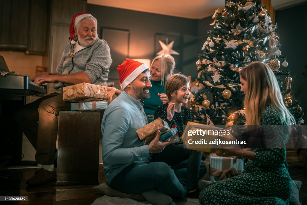 Mehrgenerationenfamilie im Wohnzimmer Weihnachtsgeschenke überreicht