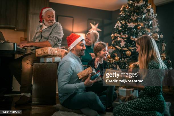 multigeneration family on the living room exchancing christmas presents - papa noel stockfoto's en -beelden