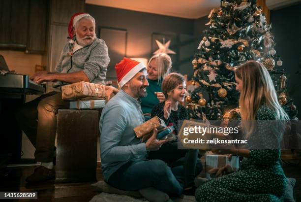 multigeneration family on the living room exchancing christmas presents - christmas gift stock pictures, royalty-free photos & images