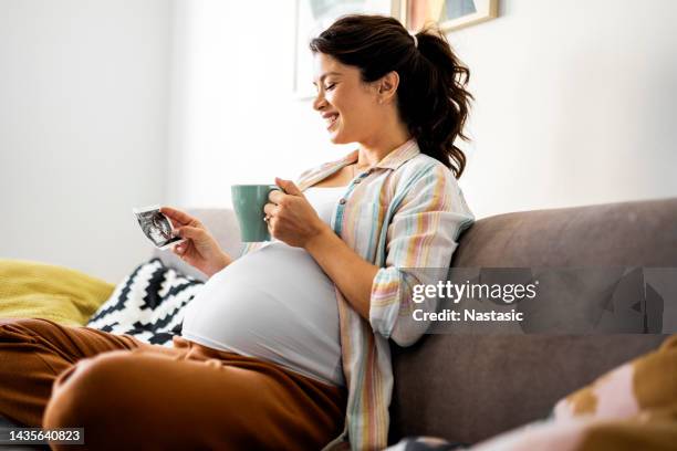 schwangere frau ruht sich aus und schaut auf baby-sonogramm - family on couch with mugs stock-fotos und bilder