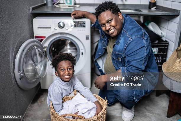 portrait of father and son washing clothes in the laundry at home - man washing basket child stock pictures, royalty-free photos & images