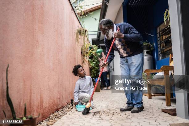 abuelo y nieto barriendo el piso del patio en casa - barre class fotografías e imágenes de stock