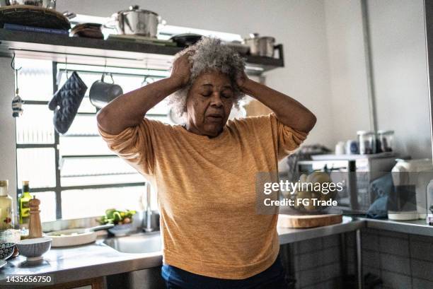 worried senior woman in the kitchen at home - grey hair stress stock pictures, royalty-free photos & images