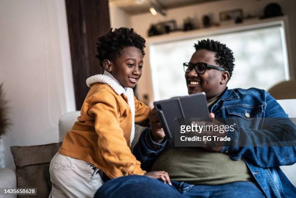 father showing something on digital tablet to his son at home - hearing aids stock pictures, royalty-free photos & images