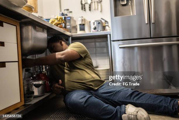 mid adult man repairing the kitchen sink at home - broken pipe stockfoto's en -beelden