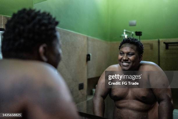 mid adult man looking himself in the mirror in the bathroom at home - obese man stock pictures, royalty-free photos & images
