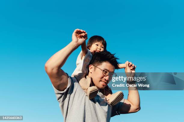 cute asian toddler on father’s shoulders against blue sky - young family stock pictures, royalty-free photos & images