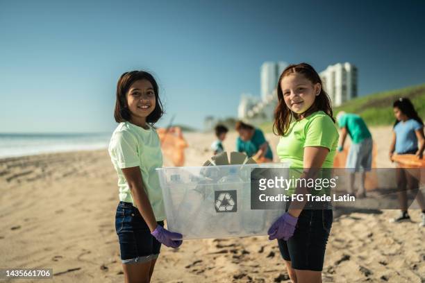 portrait of children recyclers with plastics in a bin at the beach - plastic pollution beach stock pictures, royalty-free photos & images