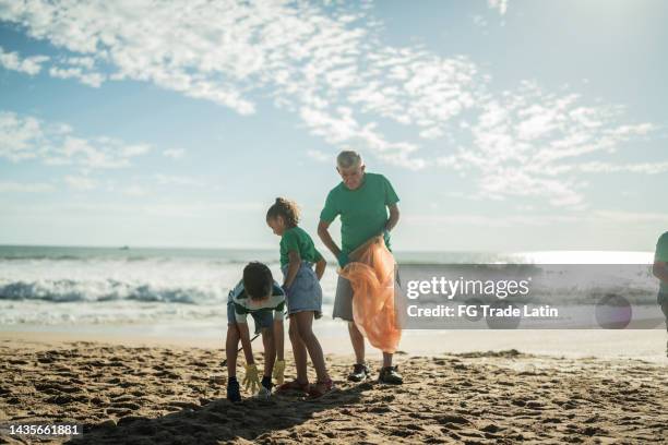 hombre mayor ayudando a los niños a recoger basura en la playa - contaminación de aguas fotografías e imágenes de stock
