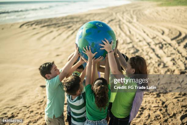 children holding a planet at the beach - world humanitarian day stock pictures, royalty-free photos & images