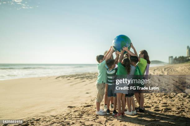 children holding a planet at the beach - earth day globe stock pictures, royalty-free photos & images