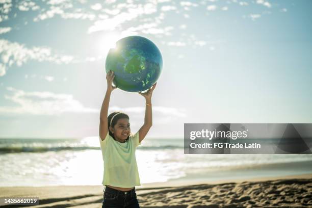 mädchen hält eine planetenkugel am strand - happy earth day stock-fotos und bilder