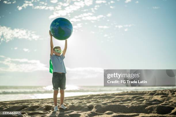 superhelden-junge hält eine erdkugel am strand - world photography day stock-fotos und bilder