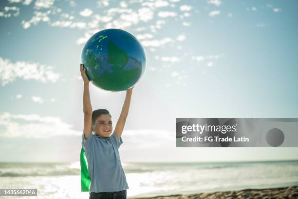 superheroe boy holding an earth sphere at the beach - child globe stockfoto's en -beelden
