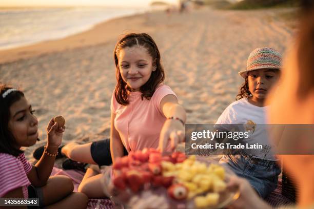 girls taking a fruit at a picnic at sunset on the beach - mexican picnic stock pictures, royalty-free photos & images