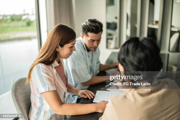 mid adult couple on a meeting with the real estate agent (or financial advisor) at home - ethnic millennial real estate stockfoto's en -beelden