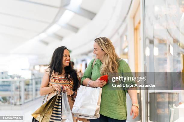 femmes souriantes portant des sacs de courses dans le centre commercial - programme de fidélité photos et images de collection