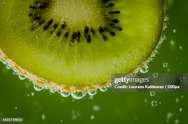 close-up of wet kiwi slice against green background - macro food stock pictures, royalty-free photos & images