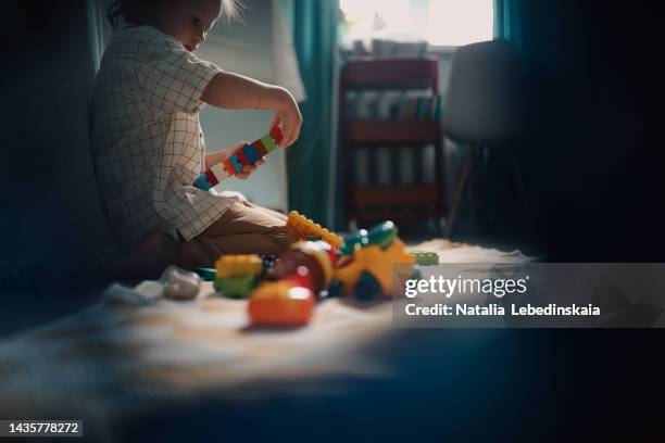 child playing in multi-colored construction set. kid builds from multi-colored blocks on floor in real interior. - kindergartengebäude stock-fotos und bilder