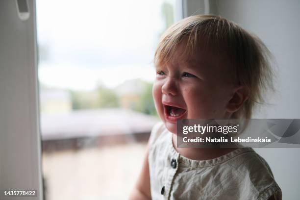 boy toddler child screams and cries at window of house. - toddler tantrum stock pictures, royalty-free photos & images