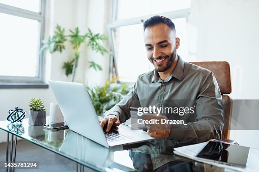 Mittlerer Erwachsener lächelnder lateinamerikanischer Geschäftsmann im Büro, mit Kreditkarte online bezahlen Mittlerer Erwachsener lächelnder lateinamerikanischer Geschäftsmann im Büro, mit Kreditkarte online bezahlen