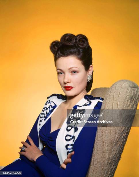 Gene Tierney vivid color studio glamour portrait in purple outfit against yellow backdrop circa 1945.