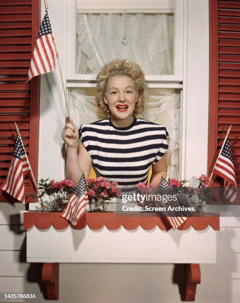 Betty Hutton waving American flag in window for a patriotic portrait circa 1944.