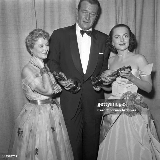 John Wayne with actresses Olivia De Havilland and Janet Gaynor at the 1952 Academy Awards holding Oscar statues.