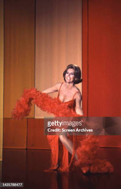 Cyd Charisse in low cut red costume and feather stole on stage circa 1960.