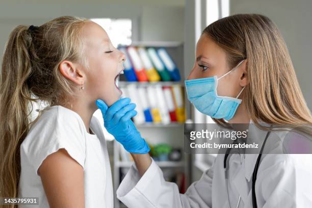 pediatrician with protective face mask examining girl's throat - human mouth stock pictures, royalty-free photos & images