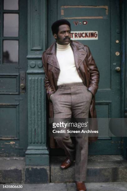 Richard Roundtree iconic portrait standing in Harlem doorway wearing classic long brown leather coat jacket as private eye John Shaft from the...