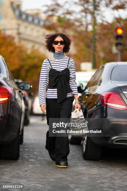 Guest wears black sunglasses, a blue large fabric with embroidered silver large metallic details, a black and white striped print pattern long...