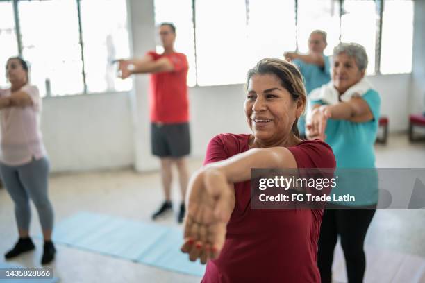 senior woman stretching with classmates in a yoga class at the studio - warm up exercise indoor stock pictures, royalty-free photos & images