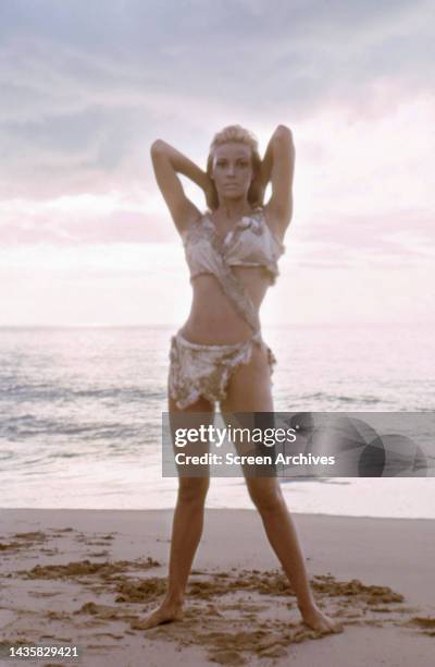 Raquel Welch striking glamour pin up pose in the famed cavegirl bikini posing barefoot on beach for the 1966 Hammer film One Million Years BC.