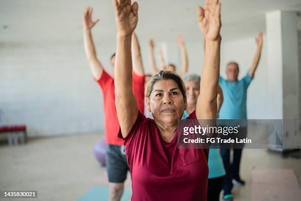 mujer mayor estirándose con compañeros de clase en el estudio de yoga - mature latin women fotografías e imágenes de stock