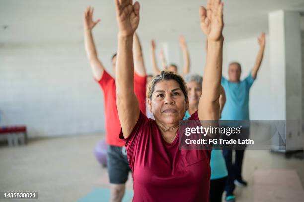 senior woman stretching with classmates at the yoga studio - woman standing exercise stockfoto's en -beelden