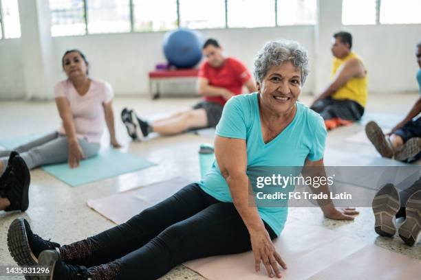 retrato de una mujer mayor estirándose en una clase de yoga en un estudio - latina legs fotografías e imágenes de stock