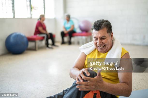 senior man feeling pain on his knee at yoga studio - male knee stock pictures, royalty-free photos & images