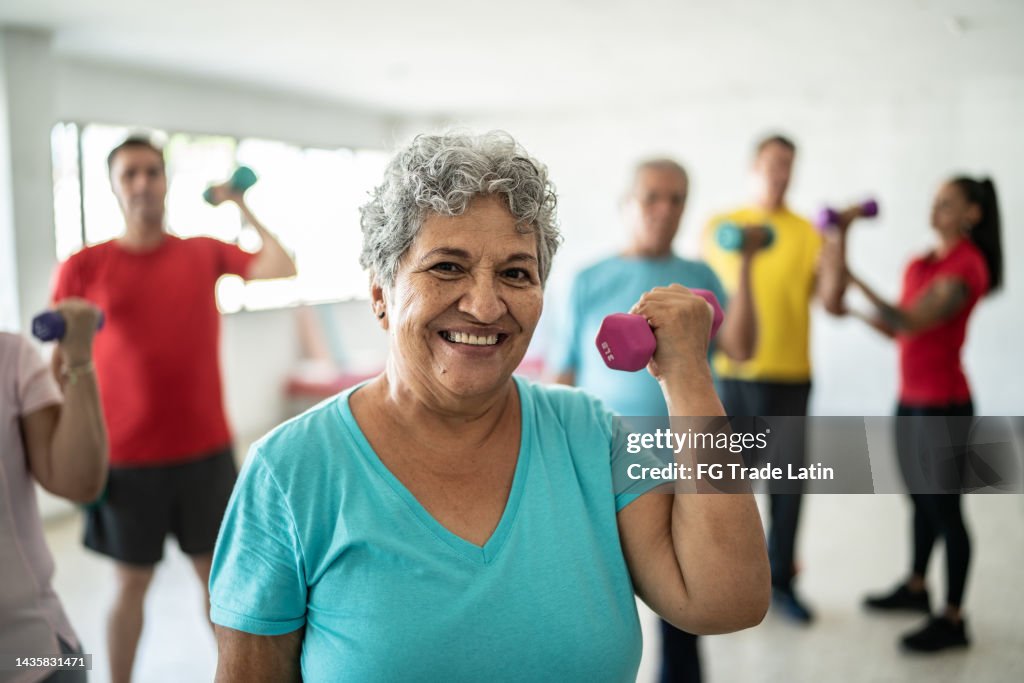 Portrait d’une femme âgée soulevant des poids avec des camarades de classe au gymnase