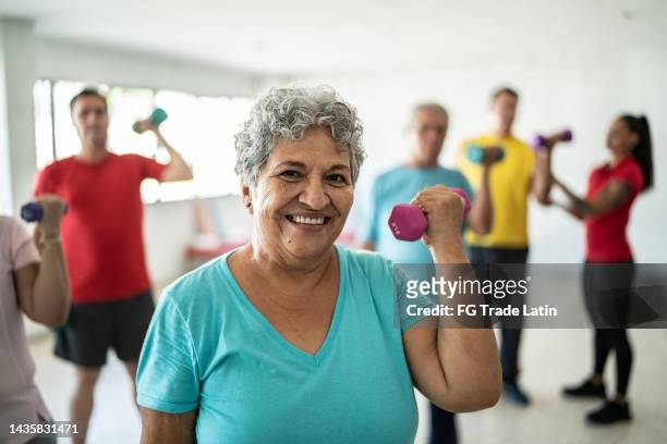 portrait of senior woman lifting weights with classmates at the gym - weightlifting imagens e fotografias de stock