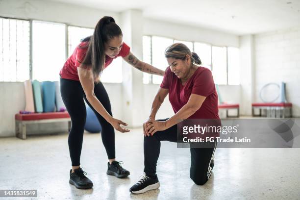 ältere frau wird von fitnesstrainer über schmerzen an ihrem knie geholfen - female knee pain stock-fotos und bilder
