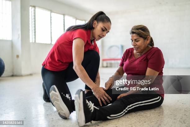 senior woman being helped by fitness instructor about pain on her knee - female knee pain stockfoto's en -beelden