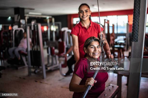 portrait of senior woman with fitness instructor pulling weight machine at the gym - personlig tränare bildbanksfoton och bilder